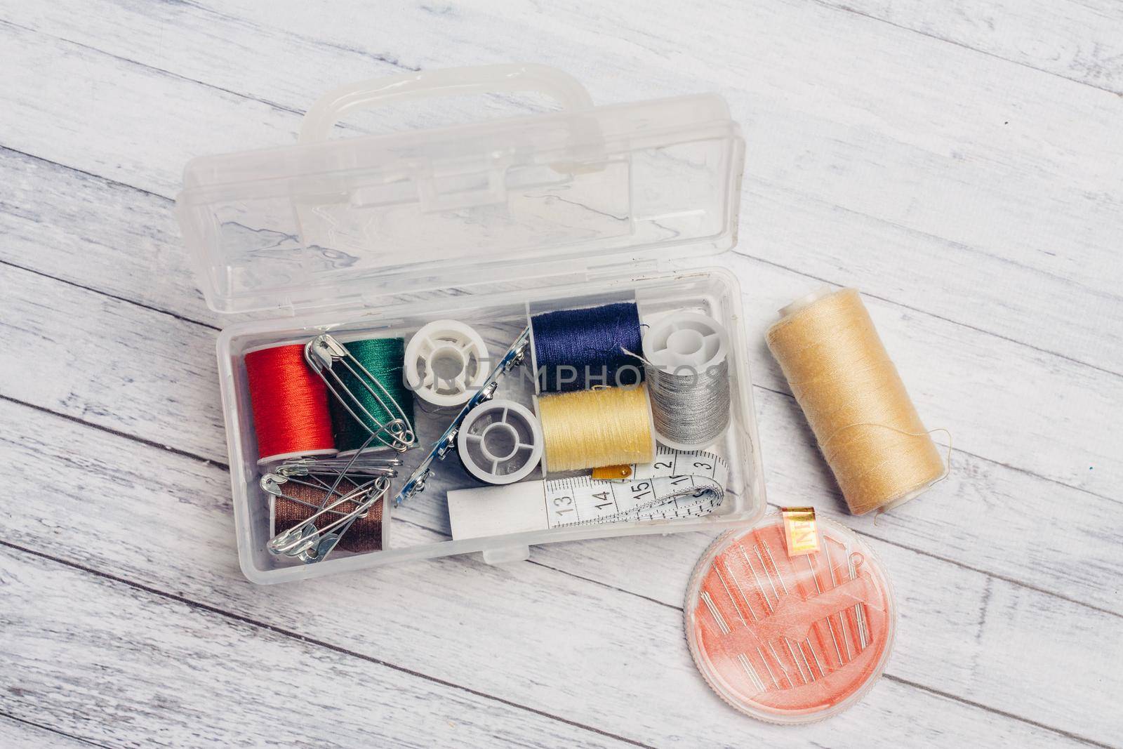 thread needles sewing supplies in a plastic box on a wooden background by SHOTPRIME