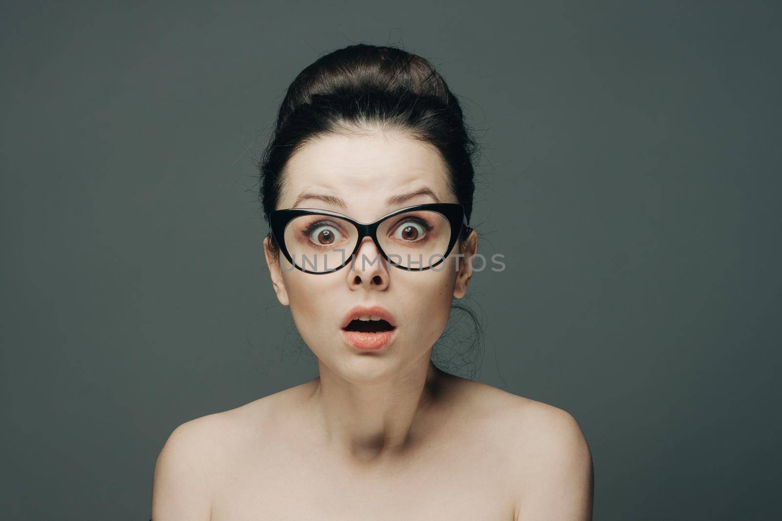 woman with glasses naked shoulders gathered hair gray background. High quality photo