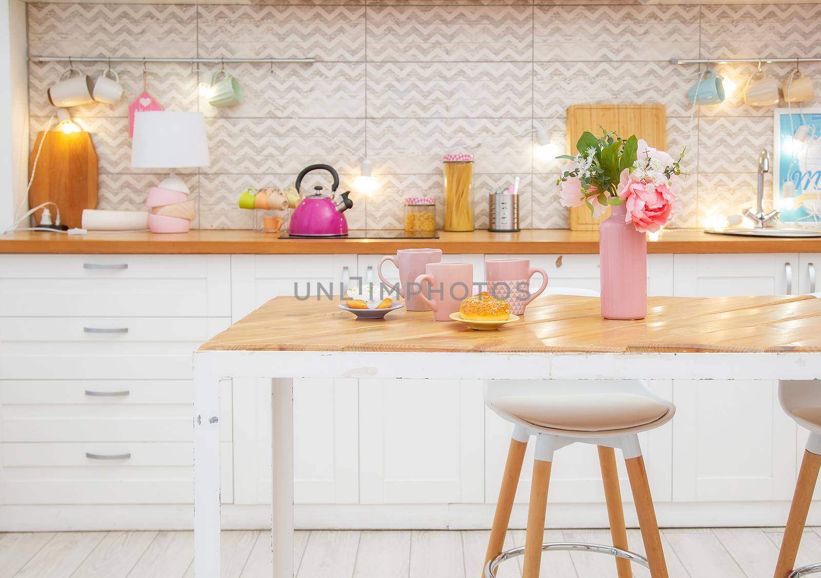 Pink vase with flowers and mugs for tea on the table in a light kitchen in the Scandinavian style.