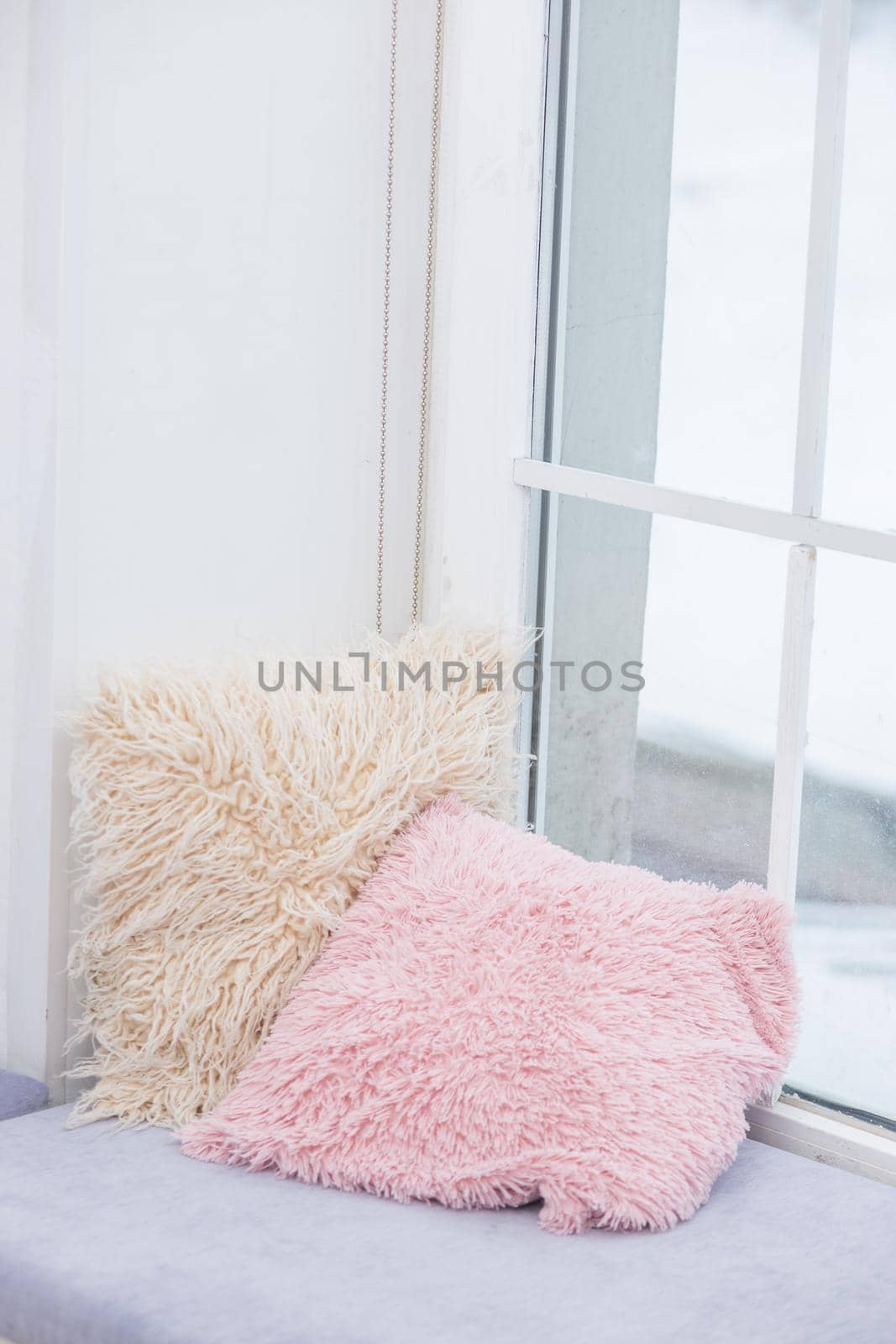 Decorative pillows with long pile pillowcases lie on the windowsill, reading area by the window