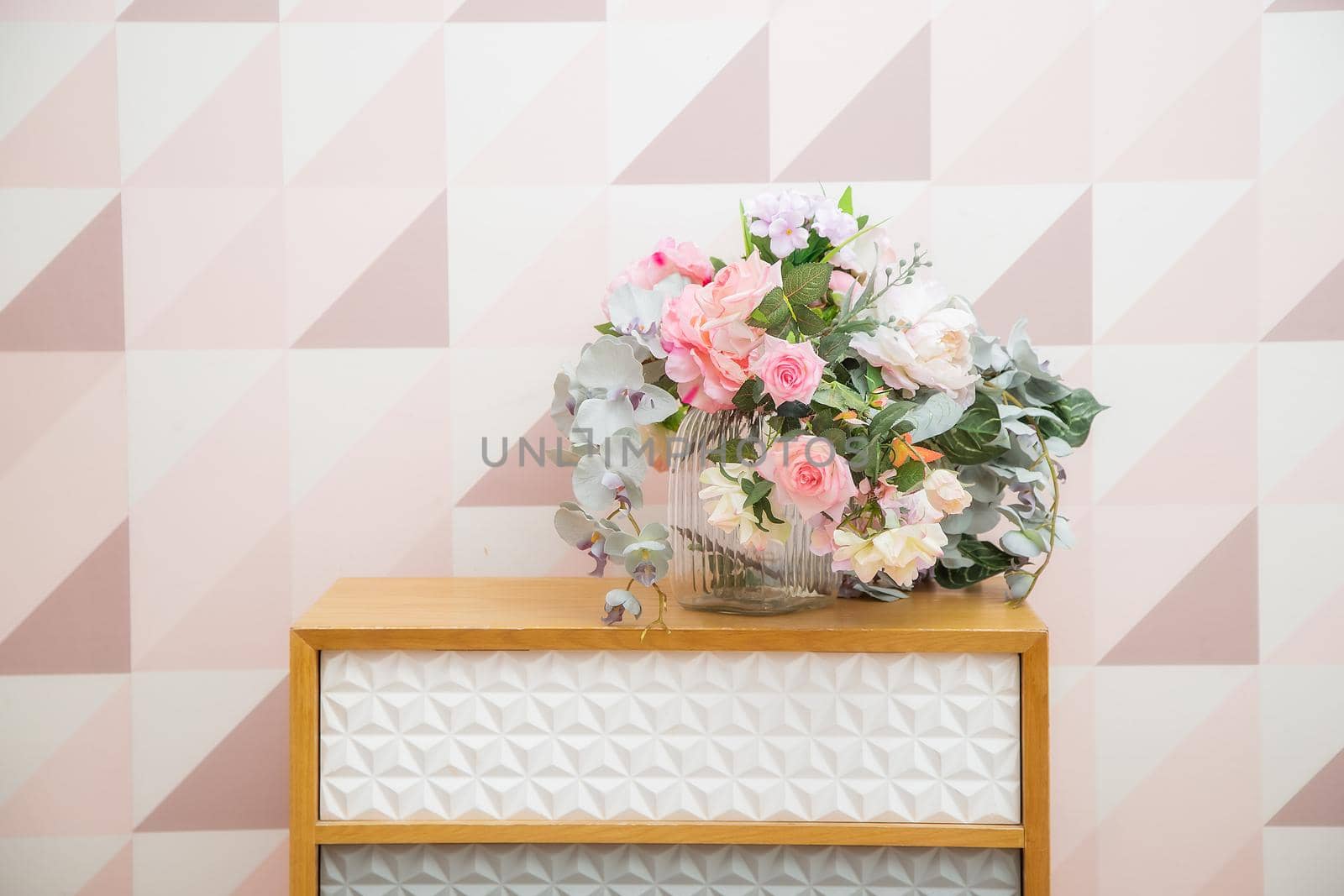 A vase of flowers on a chest of drawers near the wall with a geometric pattern by galinasharapova