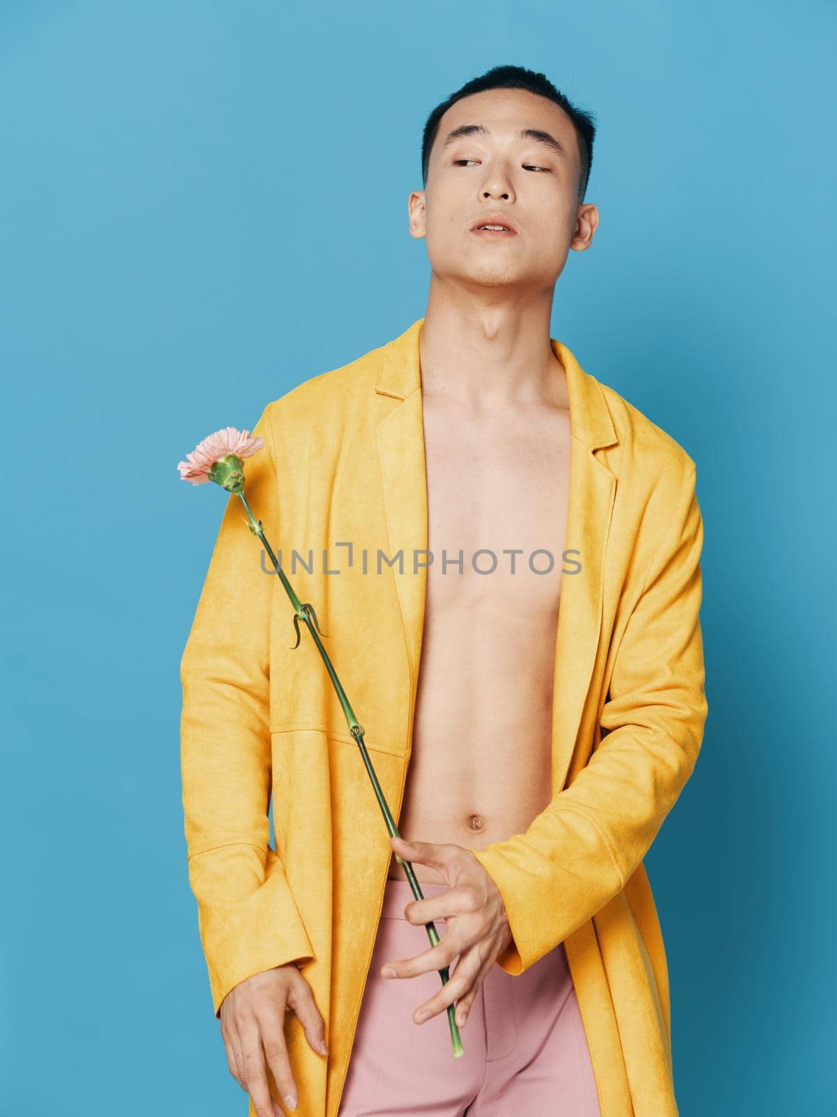 Asian guy in yellow coat holds flower in hand cropped view by SHOTPRIME