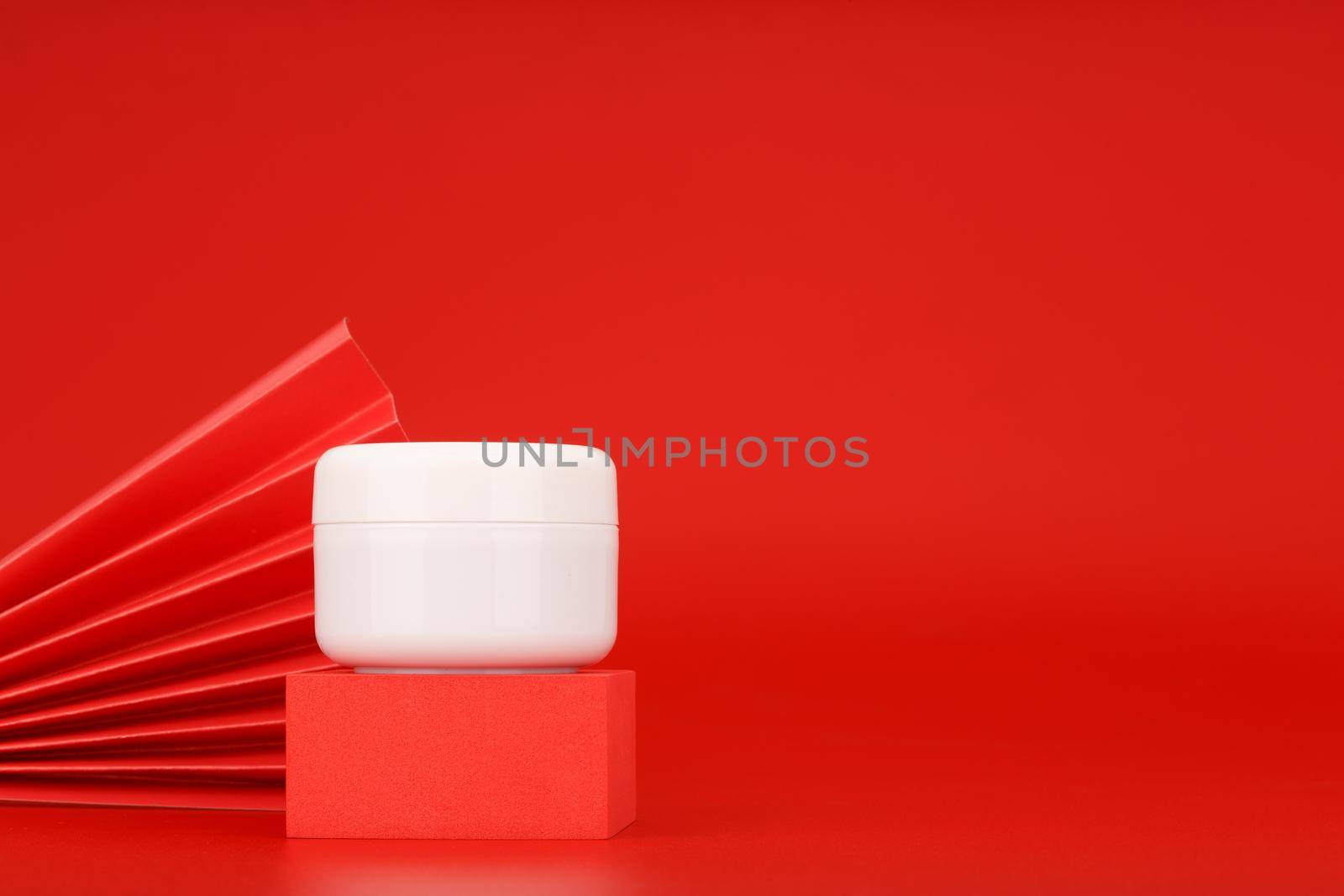 White cream jar on red podium against red background with copy space decorated with red waver. by Senorina_Irina