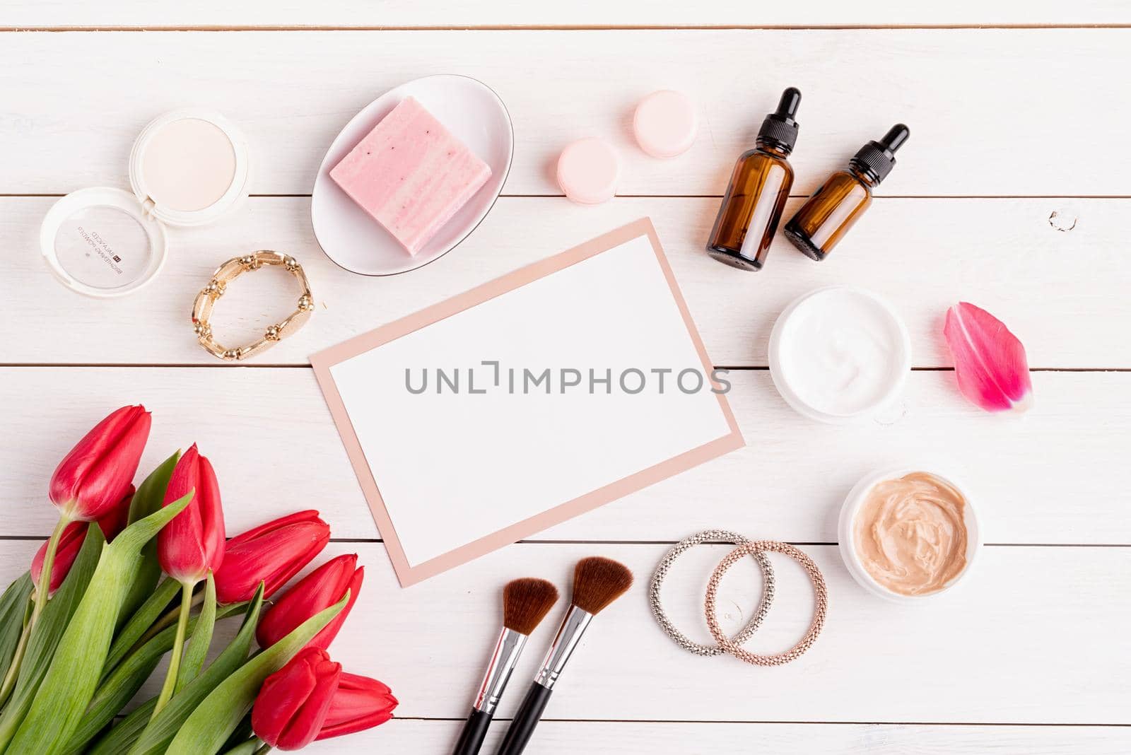 Top view of cosmetics with pink tulips top view flat lay on white wooden background by Desperada