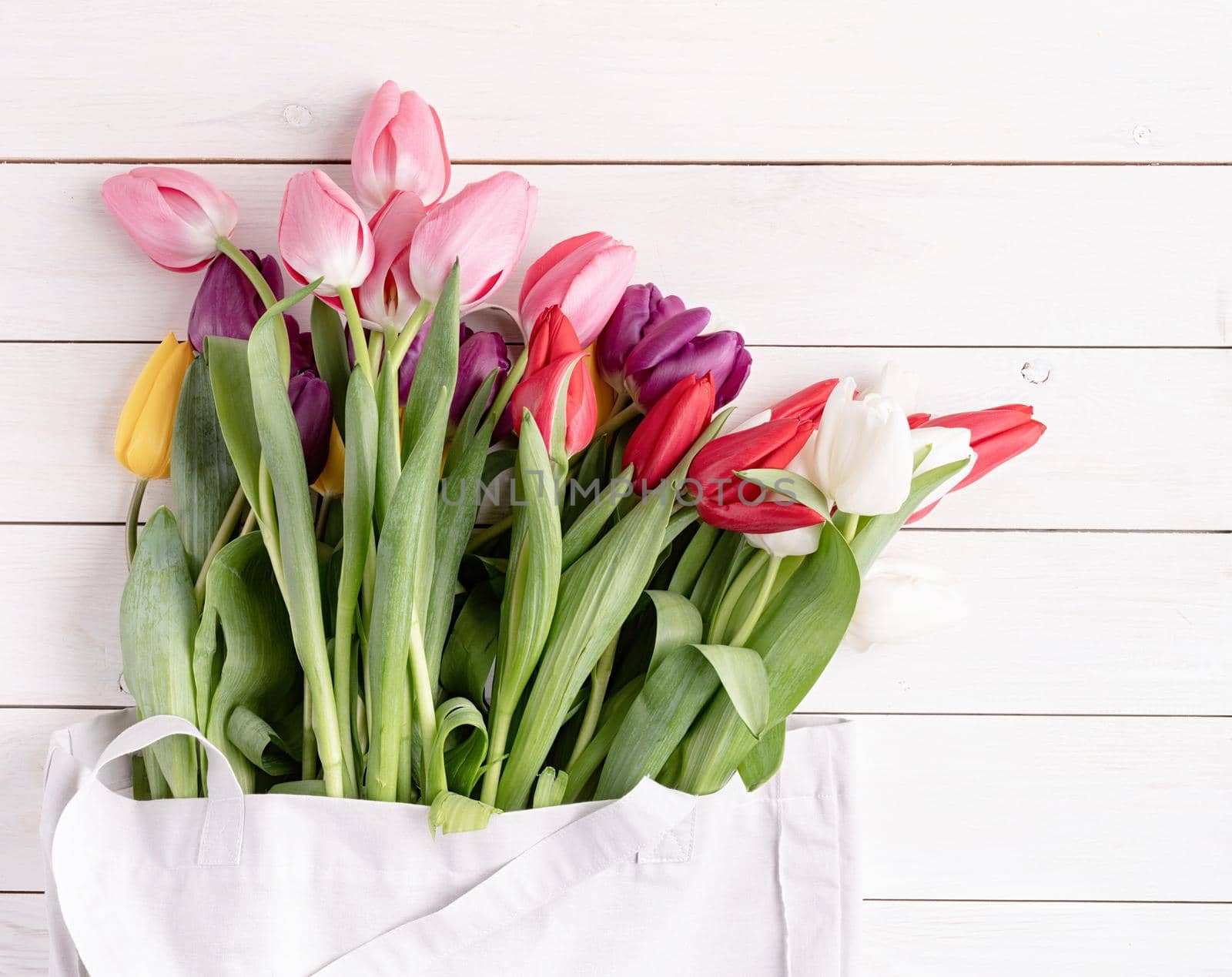 Eco friendly, zero waste concept. Gray fabric bag full of colorful tulips on white wooden background