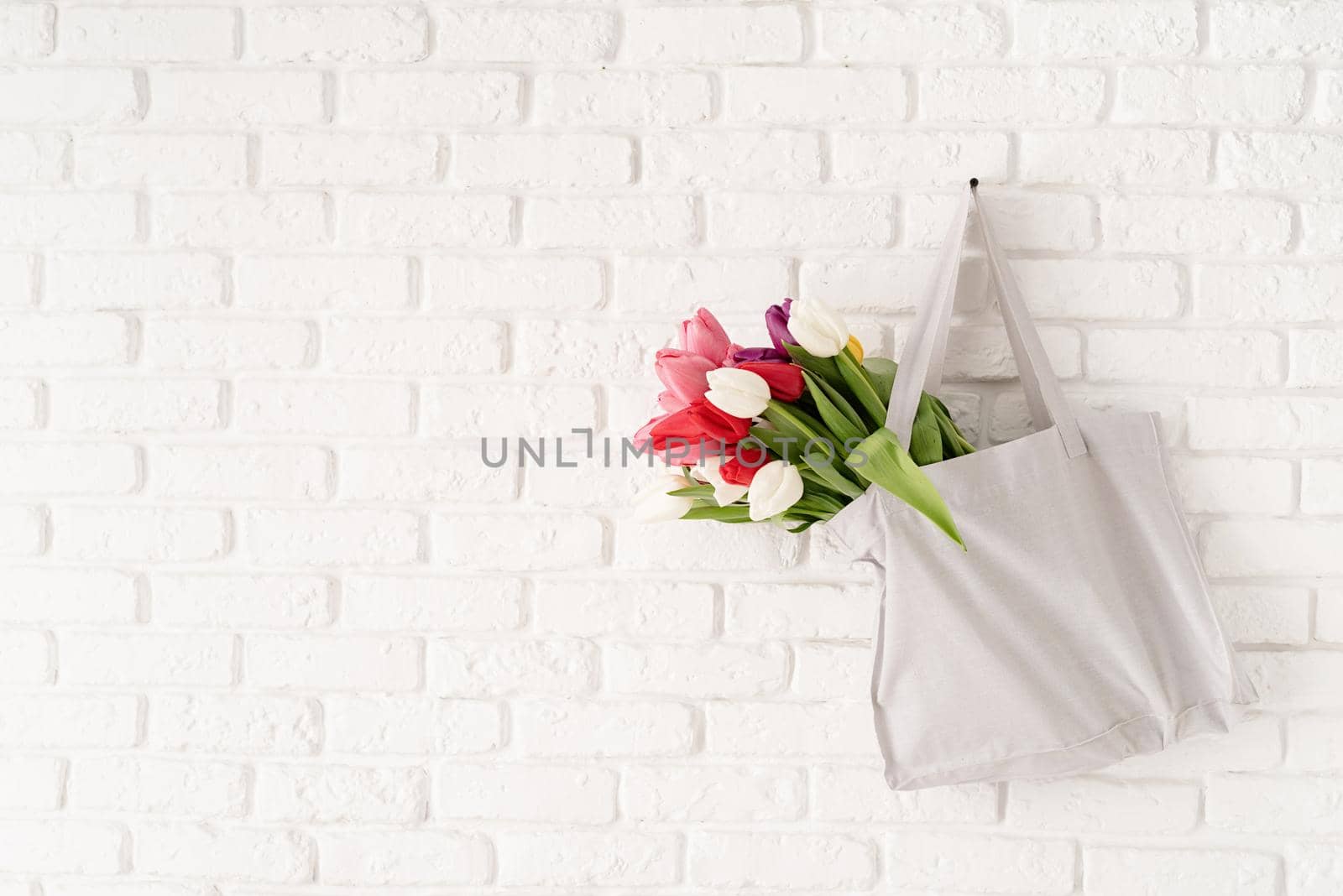 Eco friendly, zero waste concept. Gray fabric bag full of colorful tulips on white brick background