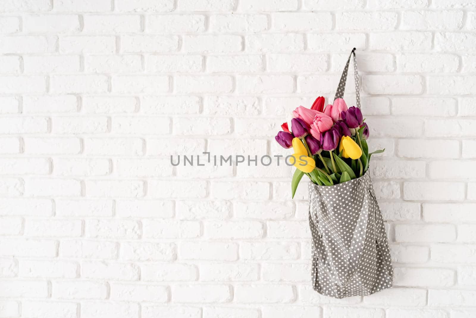 Eco friendly, zero waste concept. Gray fabric bag ful of colorful tulips on white brick background