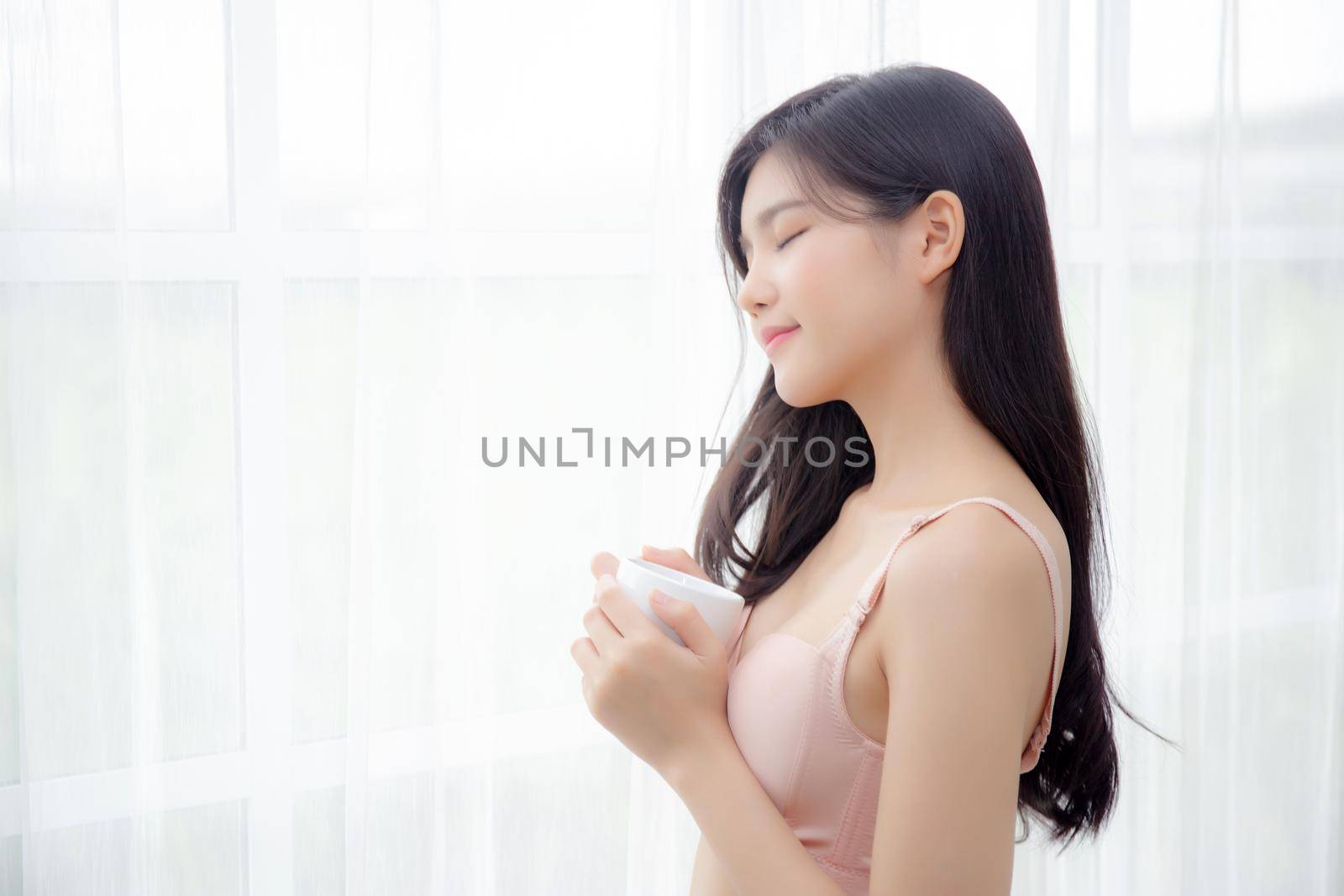 Beautiful young asian sexy woman in underwear drinking coffee near windows in the morning, girl with seductive figure fit drinking beverage for relax and resting after wake up, lifestyle concept.