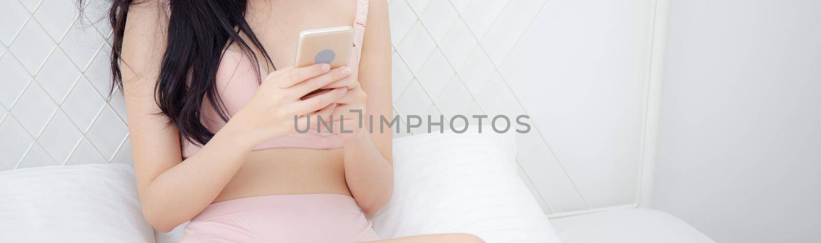 Beautiful young asian woman sexy in underwear chatting on mobile phone in the bedroom, happy girl in lingerie looking social media on smartphone for relax, communication and lifestyle concept.