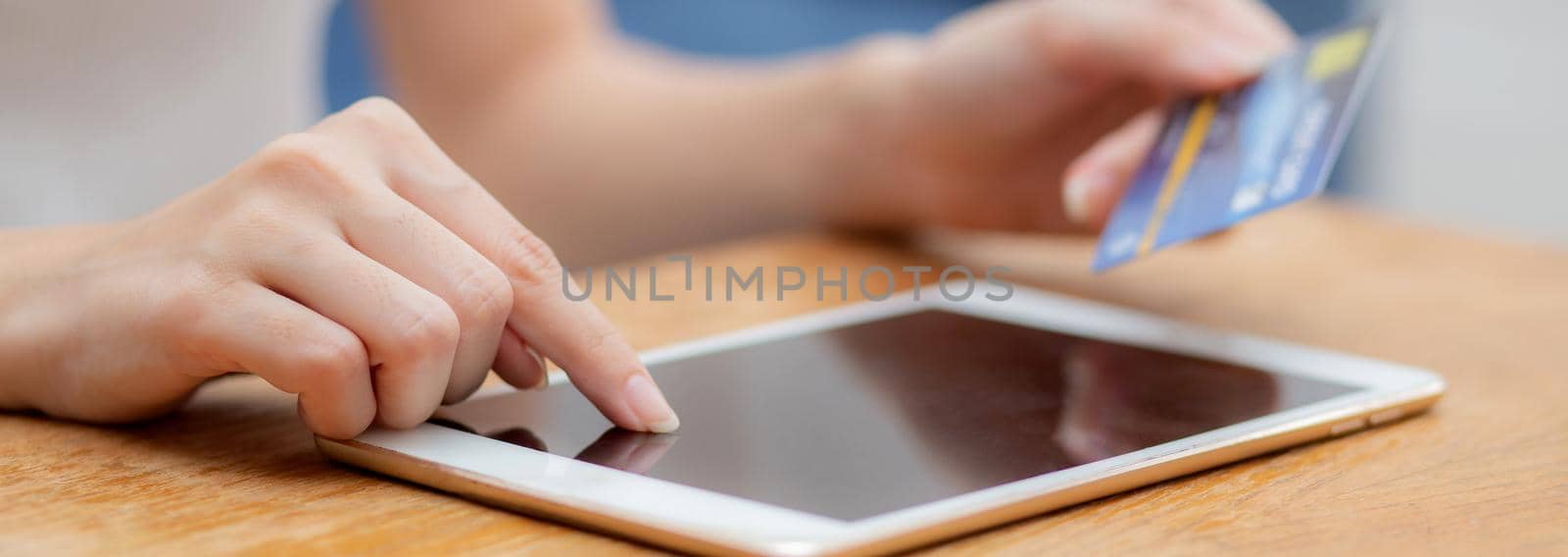 Closeup hand of young asian woman holding credit card shopping online with tablet computer blank display screen buying and payment, girl using debit card purchase or transaction, e-commerce concept.