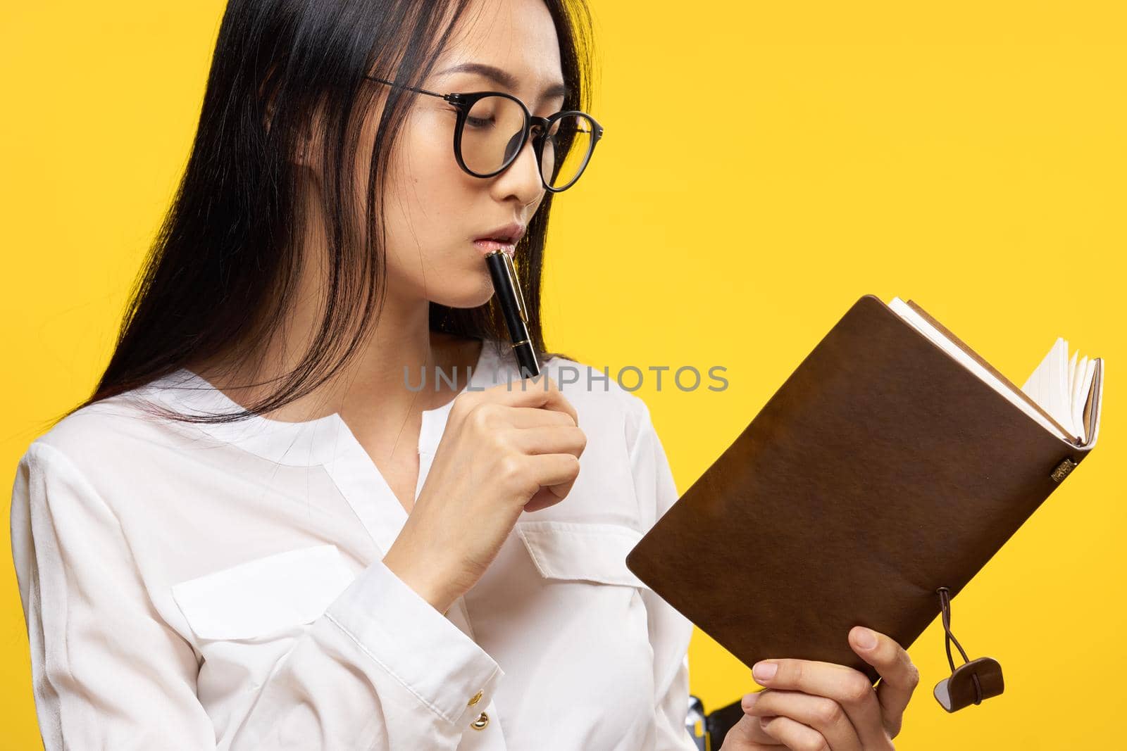 woman of asian appearance looking at notepad pen in hand an official yellow background. High quality photo