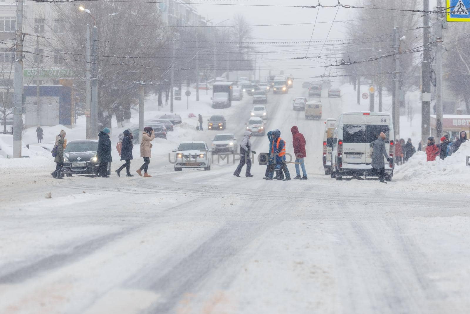 Tula, Russia - February 13, 2020: People crossing city road during heavy snow fall at day light.