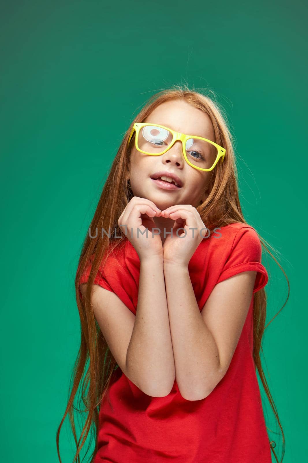 cute red-haired girl with glasses gesturing with her hands school childhood green background. High quality photo