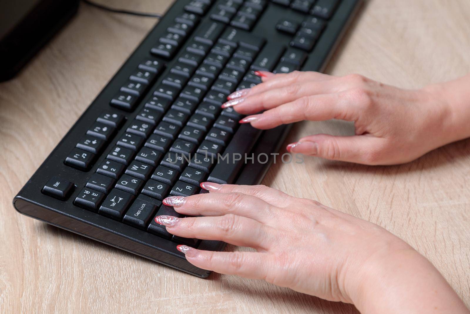 A woman director working in an office is sitting at a table, typing on a keyboard, checking documents. Close-up.