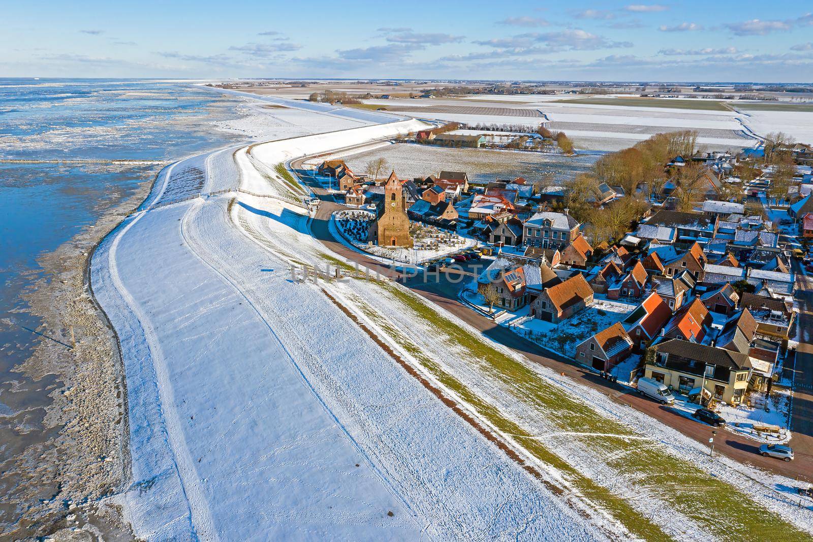 Aerial from snowy village Wierum in Friesland at a frozen Waddensea in the Netherlands in winter by devy