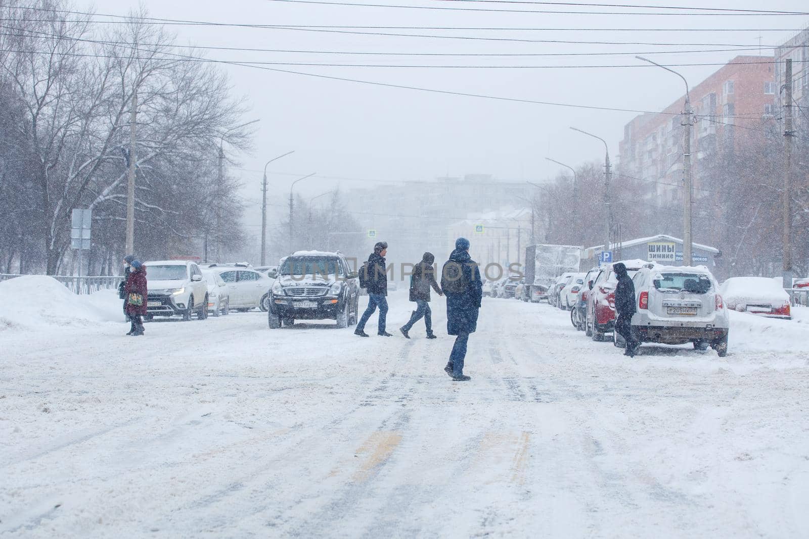 Tula, Russia - February 13, 2020: Citizens crossing city road during heavy snow fall. by z1b