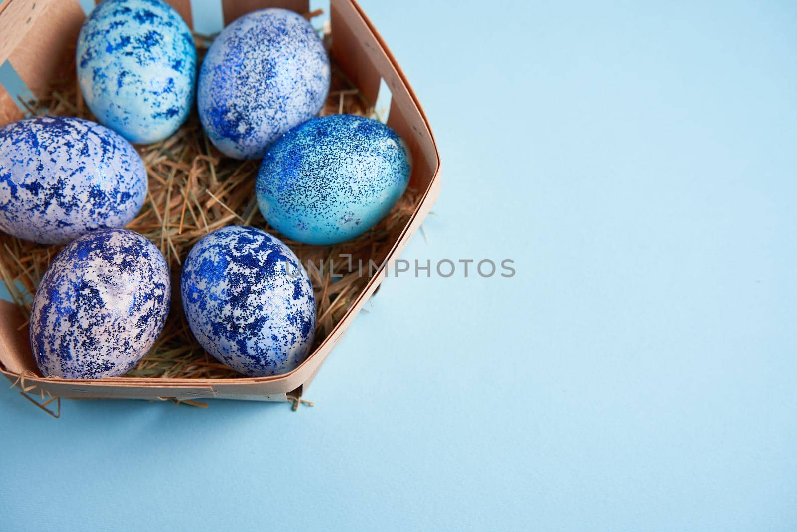 Blue chicken eggs lie in round wooden basket which stands on a blue paper background. Easter background. Seasonal holiday flat lay with free space for text. Classic blue color of the year 2020