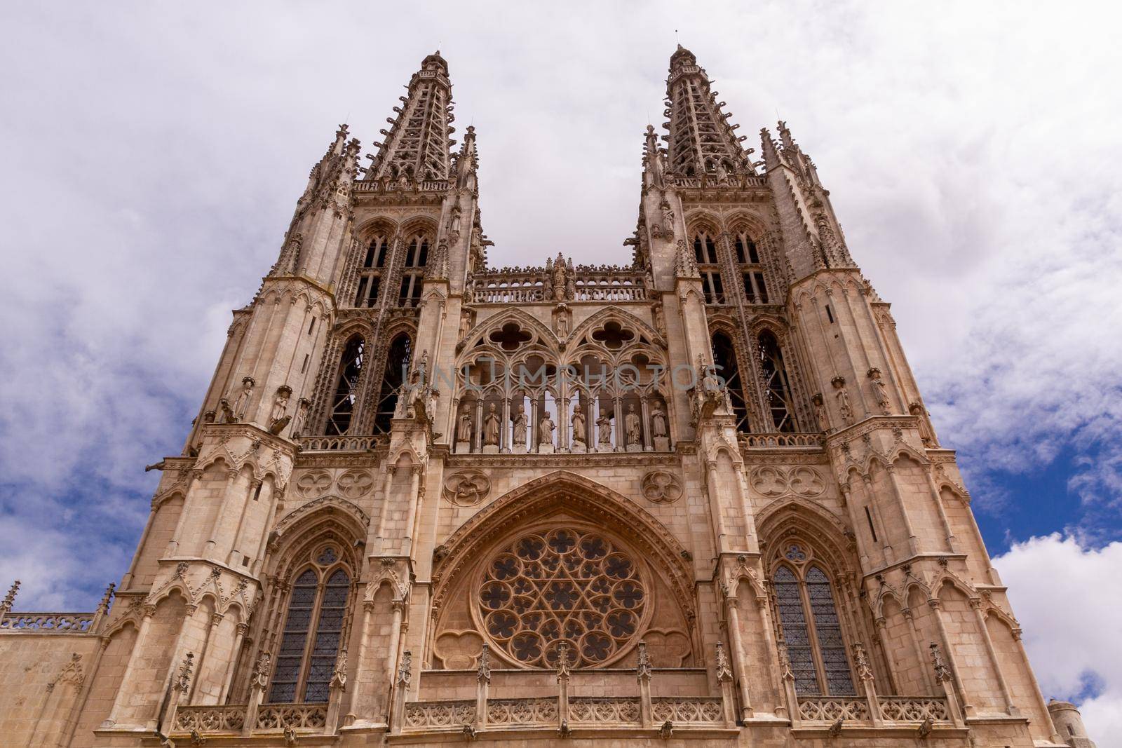 Low-angle shot of Burgos' Cathedral main facade and towers against a cloudy blue sky