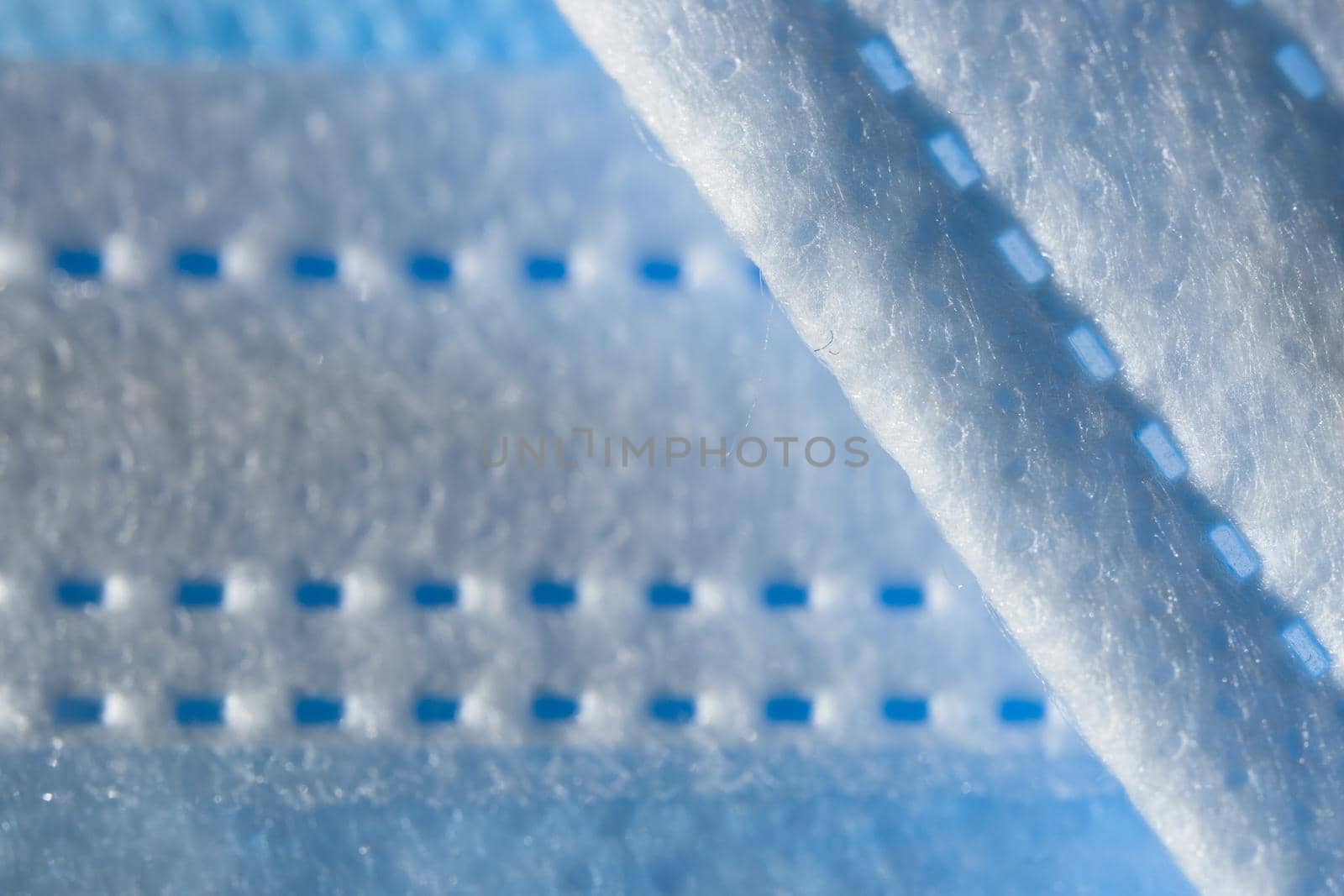 Disposable 3-ply face mask in blue color abstract background. Focus on foreground with plenty of copy space. Micro detail of medical face covering.