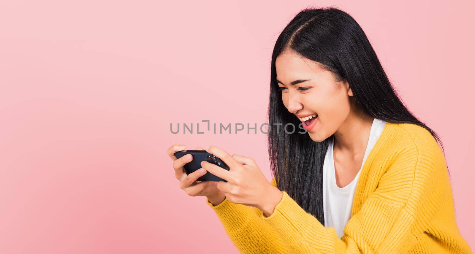 Happy Asian portrait beautiful cute young woman teen smiling excited   using mobile phone say yes! Studio shot isolated on pink background, Thai female surprised make winner gesture on smartphone