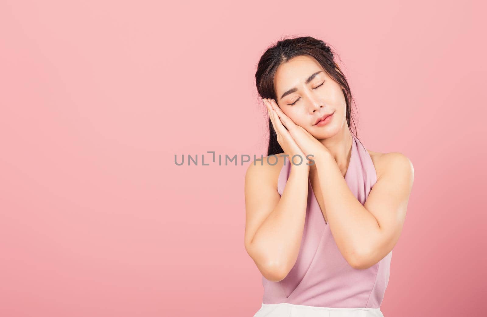 Portrait Asian beautiful young woman pretended emotions sleeping tired eyes closed dreaming with hands together near face, studio shot on pink background, with copy space, insomnia concept