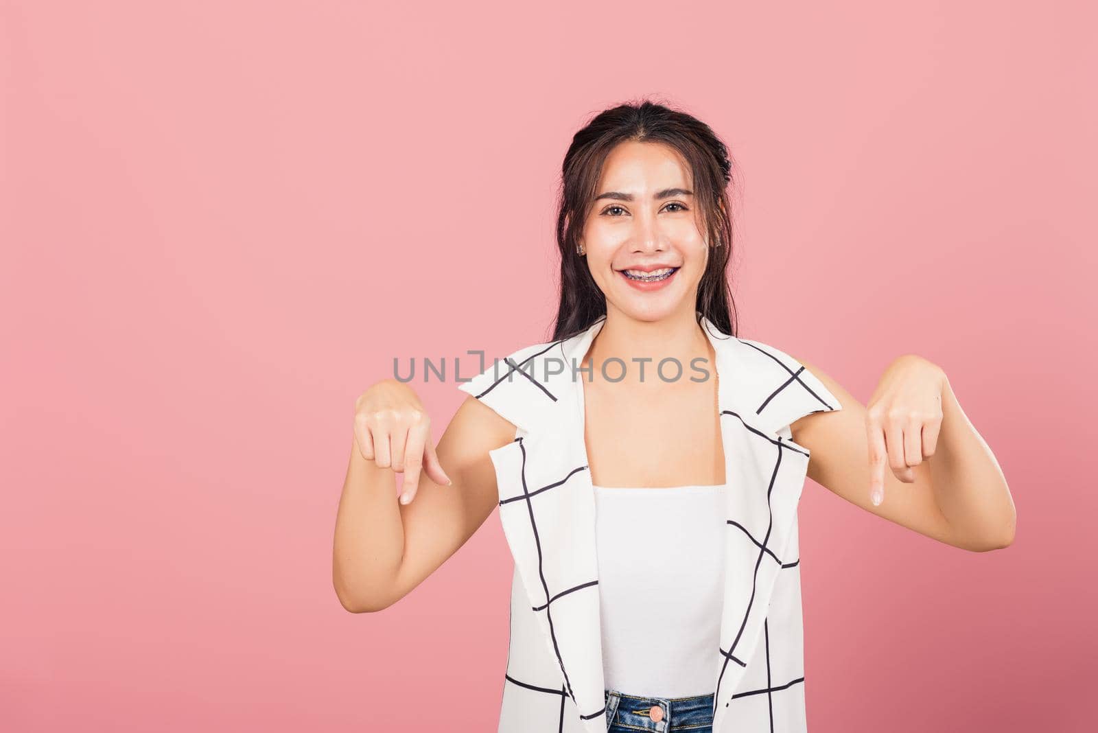 Portrait Asian beautiful young woman unhappy, negative gesture showing finger thumbs down or dislike sign, studio shot isolated on pink background, Thai female rejection unlike with copy space