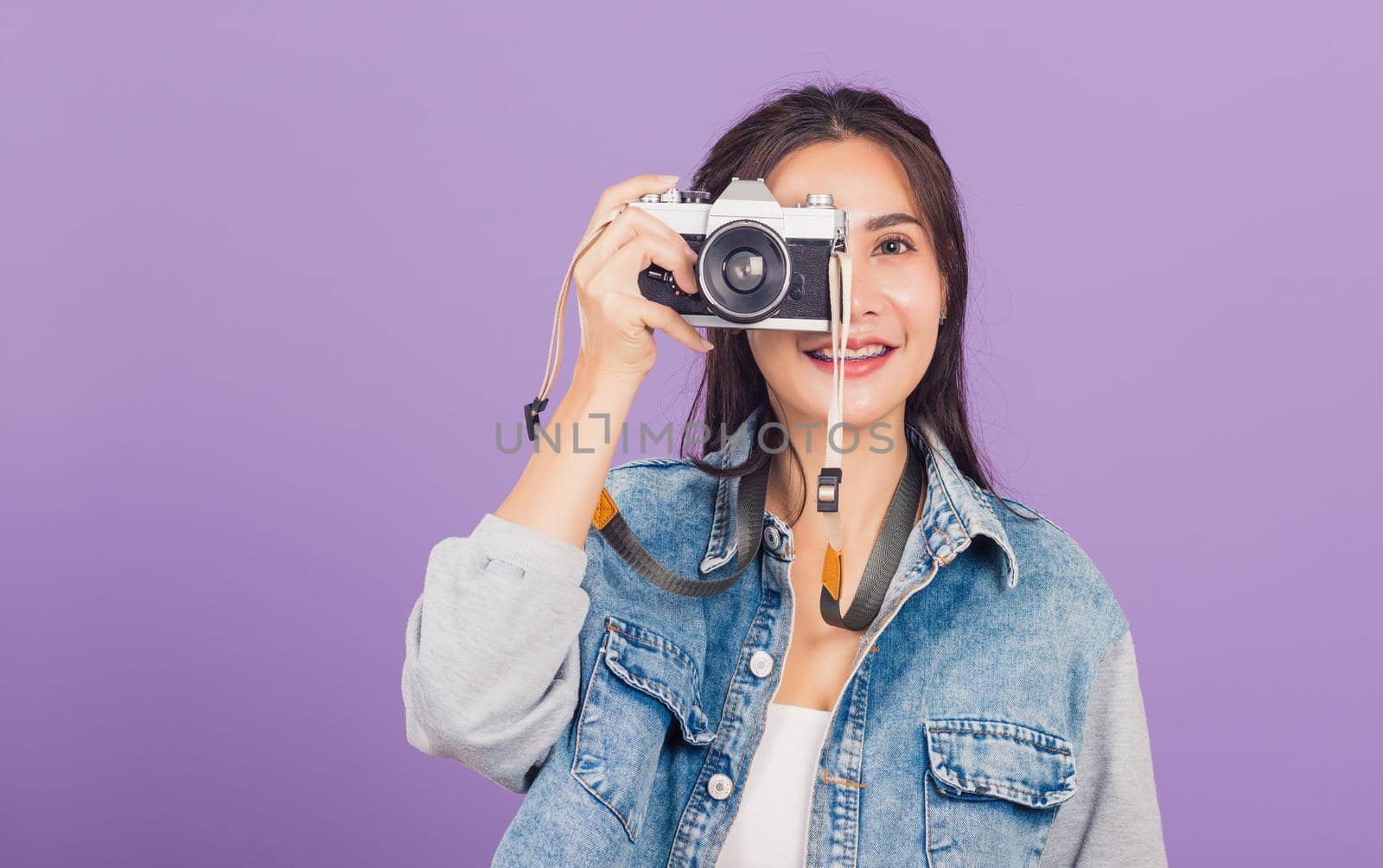 Portrait happy beautiful young woman smile excited wear denims photographer taking a picture and looking viewfinder on vintage photo camera ready to shoot, studio shot isolated on purple background