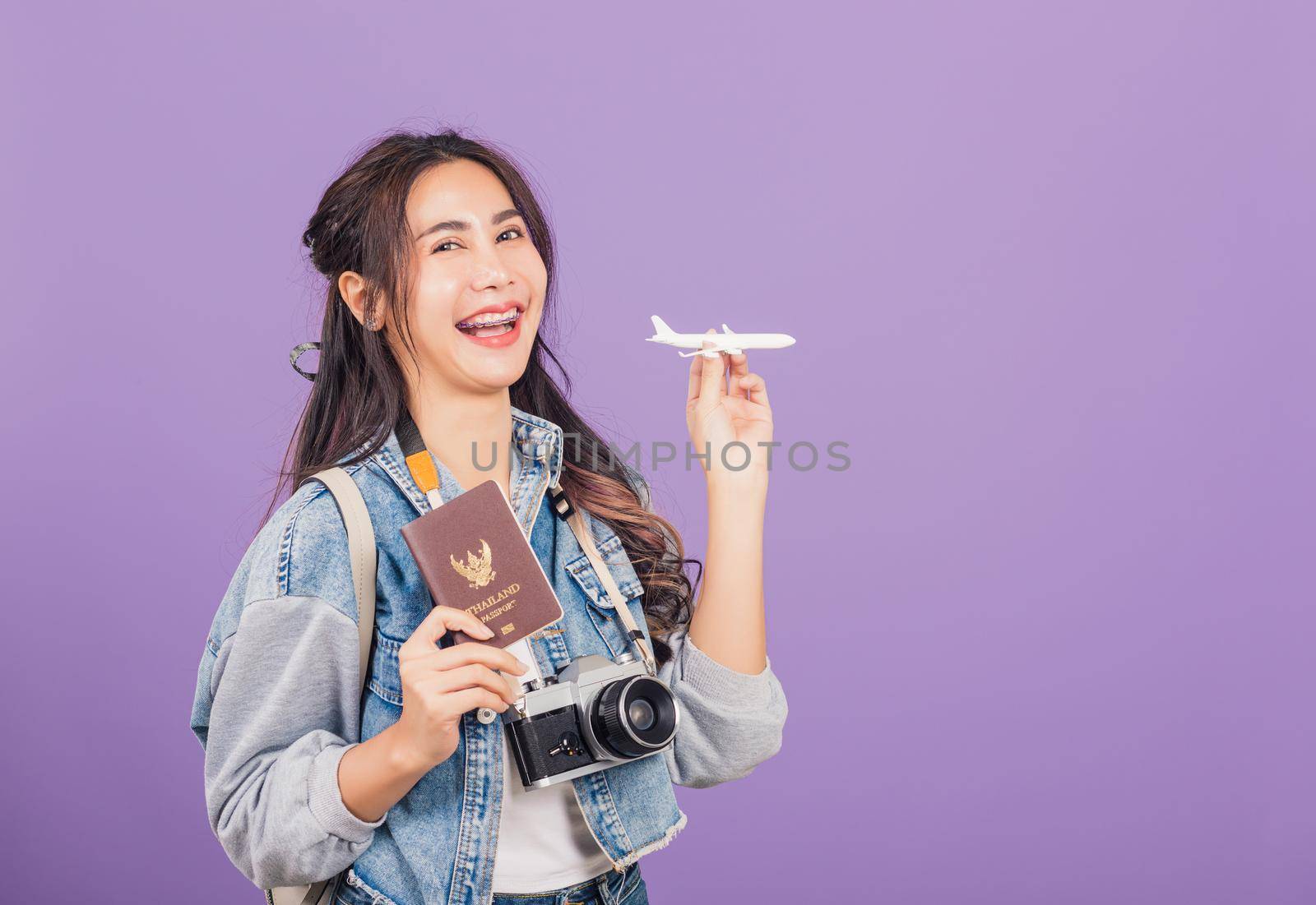 woman excited smiling in summer vacation holding airplane toy, passport and vintage photo camera by Sorapop