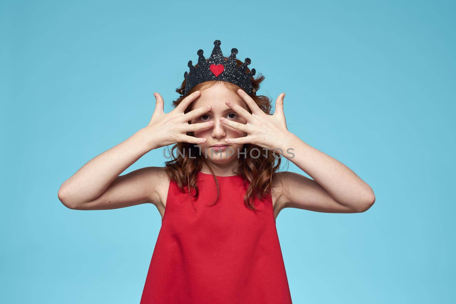 Girl with curly hair with a crown on her head red dress lifestyle blue background. High quality photo