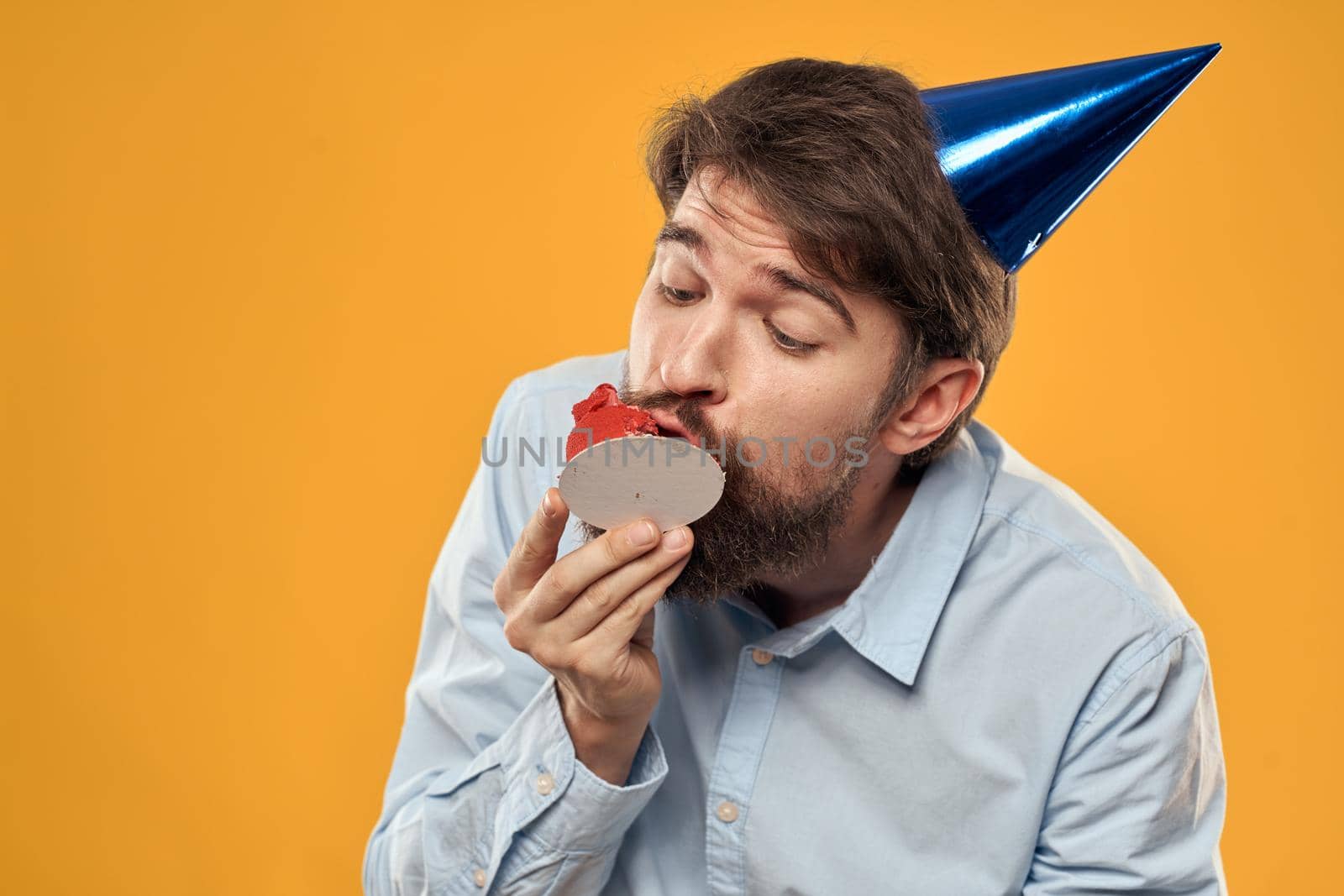 a man with a birthday cake in his hands and in a cap on a yellow background on his birthday. High quality photo