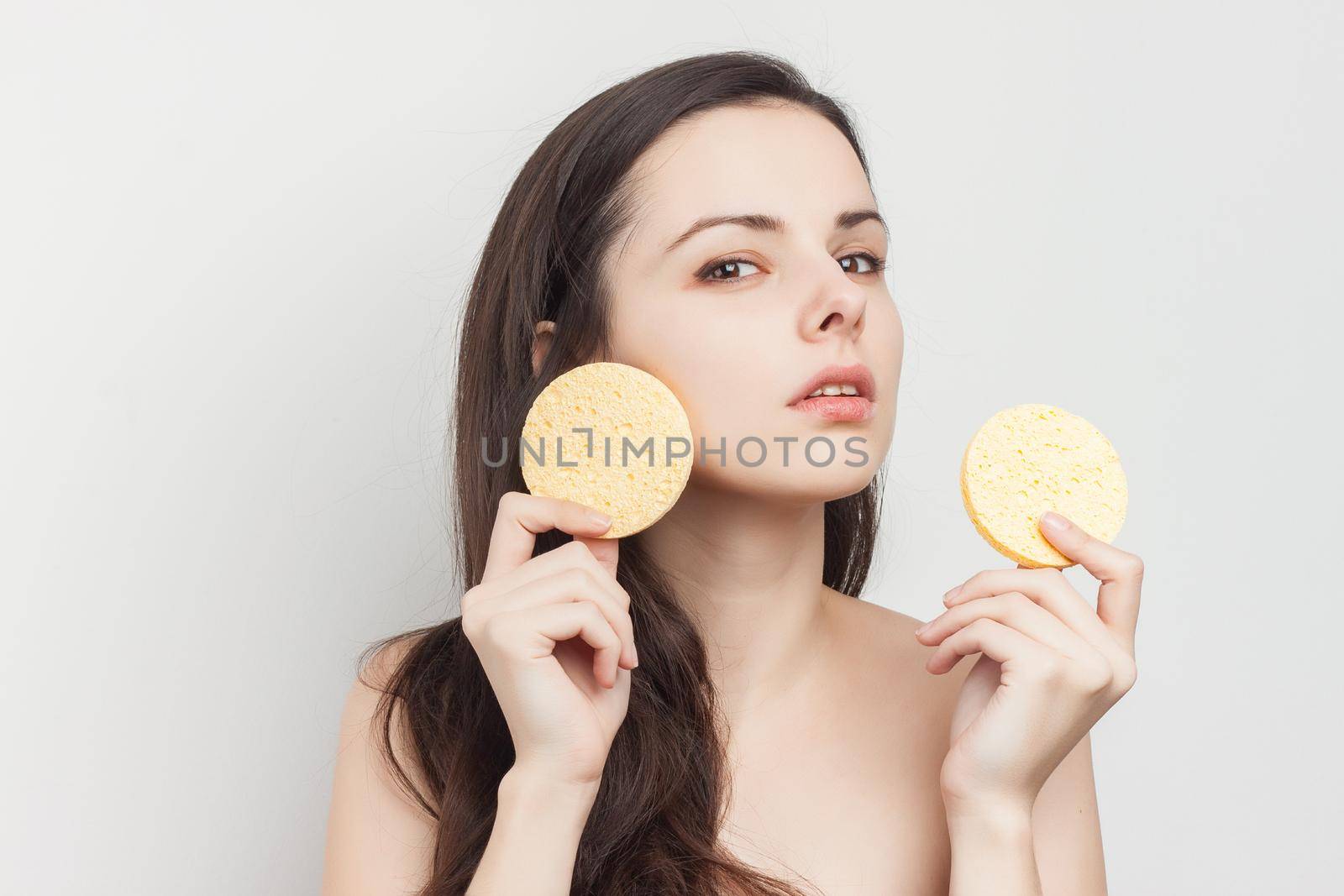 brunette naked shoulders wipes her face but clean skin with a sponge. High quality photo