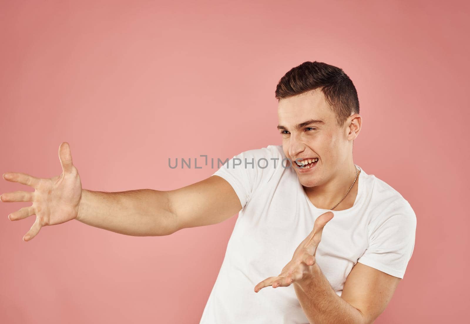emotional man in white t-shirt gesturing with hands cropped view pink background. High quality photo