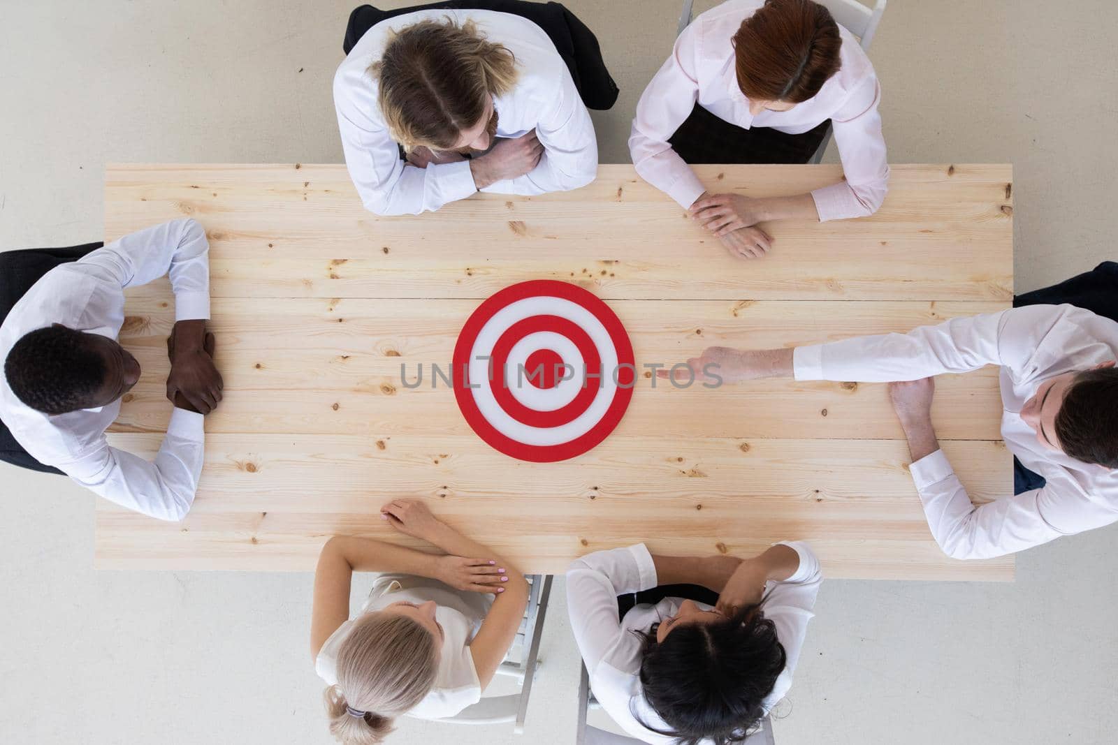 Team of business people pointing at red goal target at meeting table aiming strategic marketing on dartboard bullseye targeted creative idea achievement strategy development concept