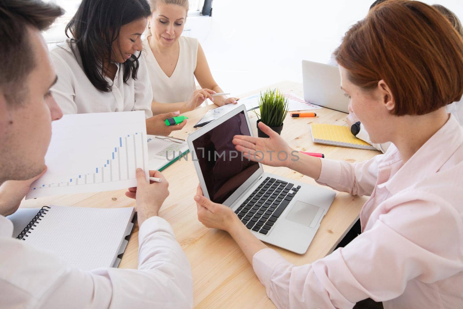 Diverse executive business people team discussing work results at meeting, multiracial businessmen talking analyzing financial statistics report sitting together in modern office with laptop and documents