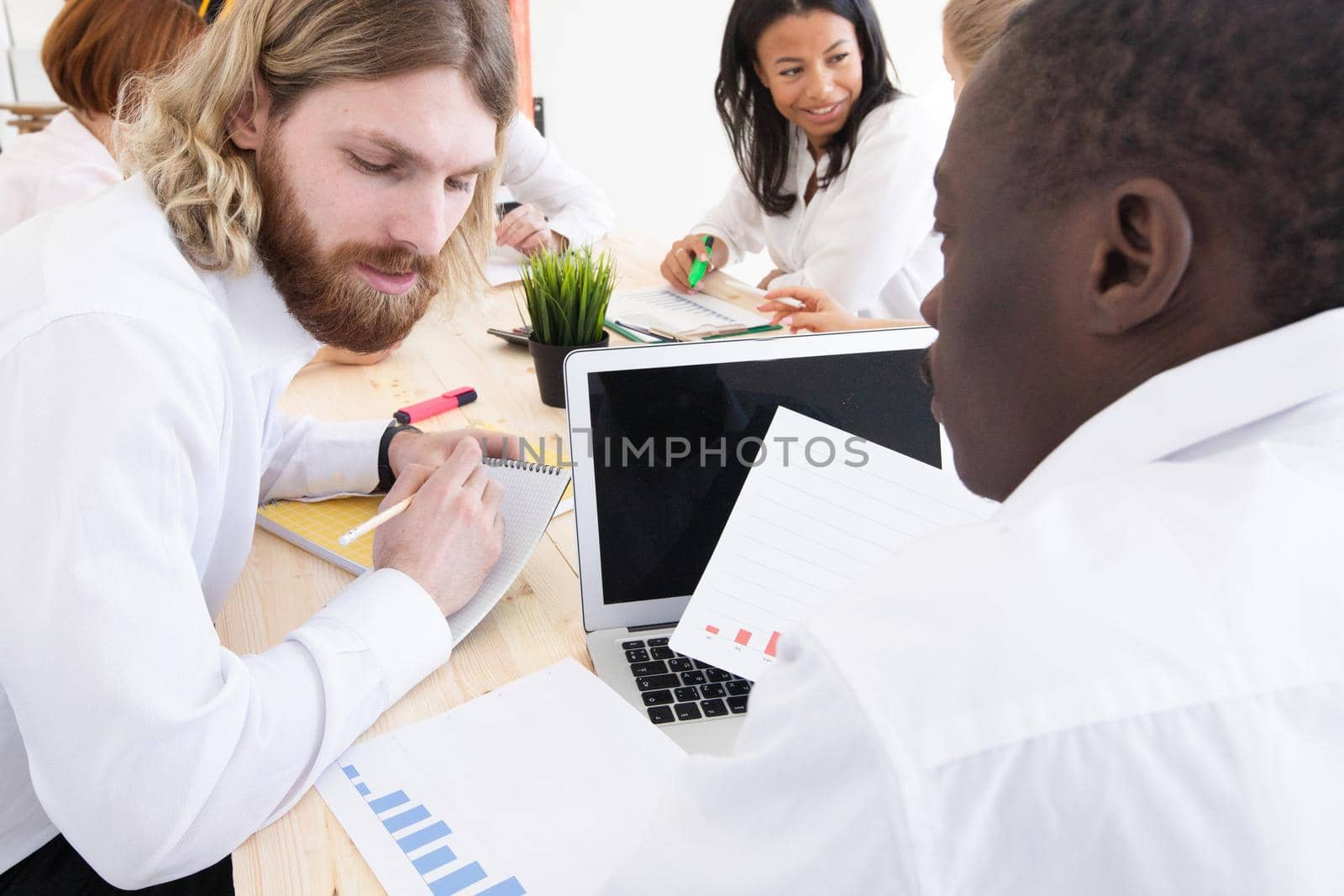 Diverse executive business people team discussing work results at meeting, multiracial businessmen talking analyzing financial statistics report sitting together in modern office with laptop and documents