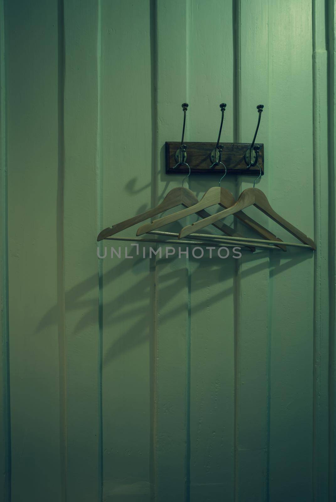 Brown wooden cloth hanger with shadow hanging on metal hook on wooden wall background. Empty coat hanger in white vintage room. Hook install on wood wall in dark room. Rustic style fitting room.