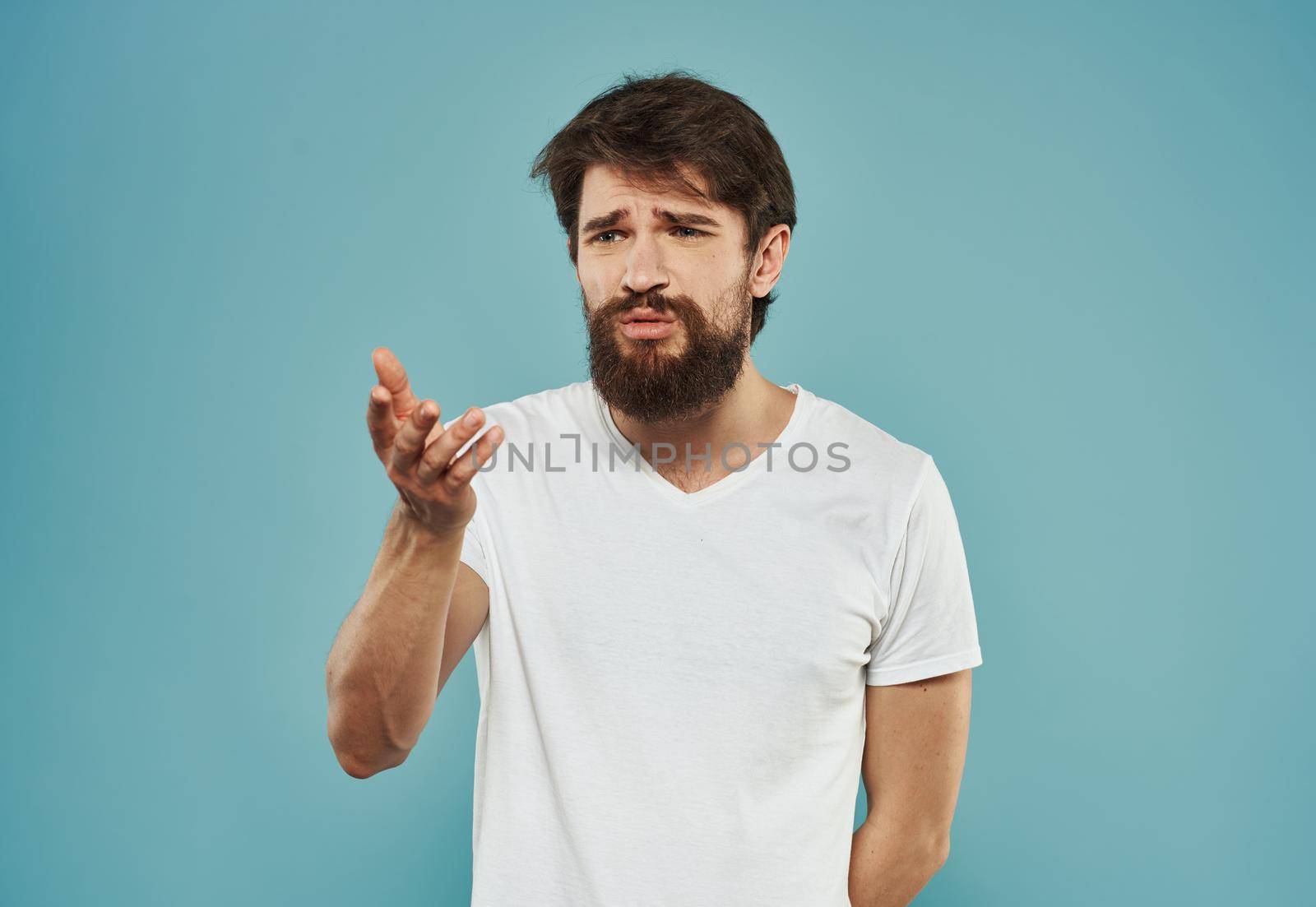 A brunette guy with a thick beard on a blue background gestures with his hands cropped view. High quality photo