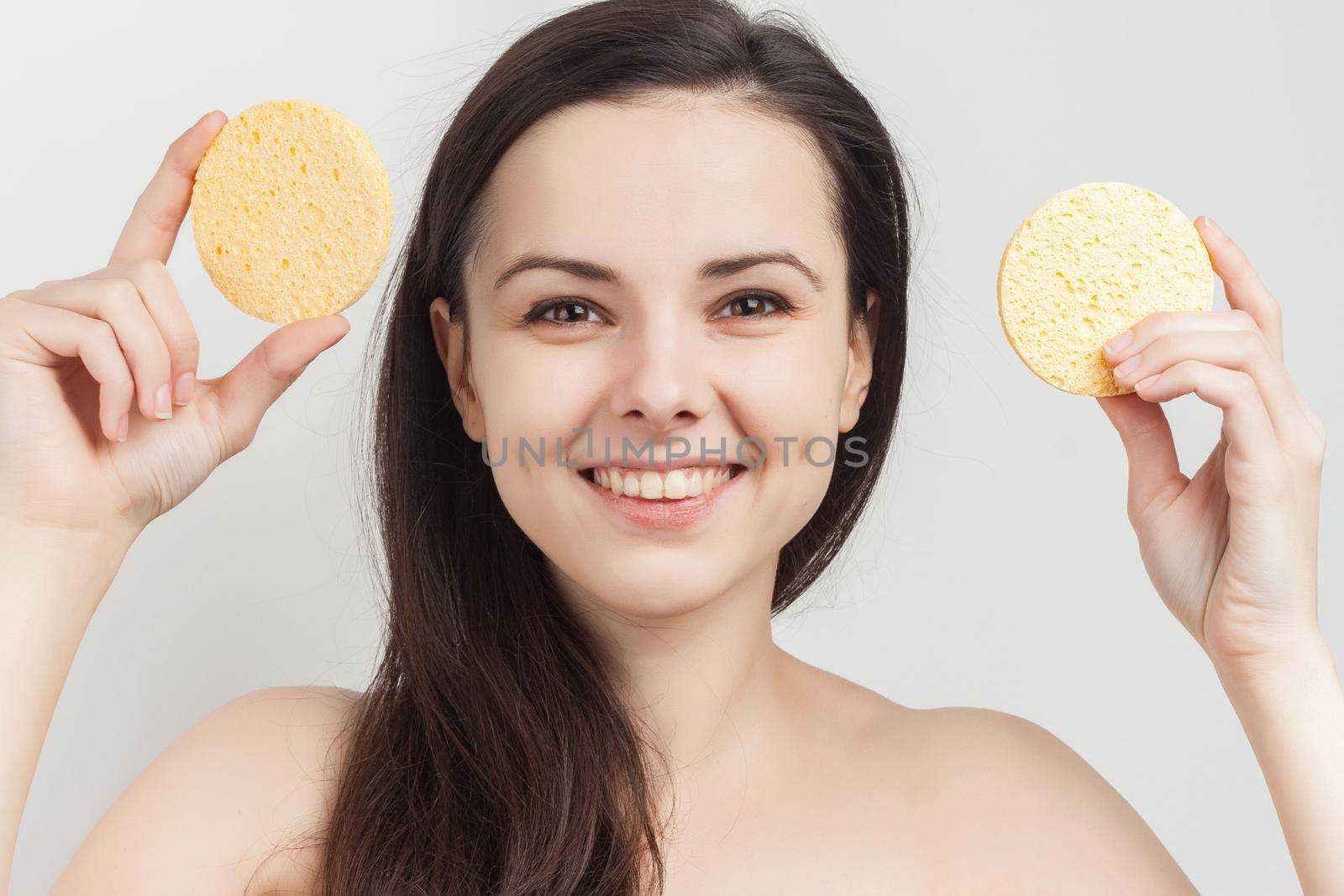brunette naked shoulders wipes her face but clean skin with a sponge. High quality photo