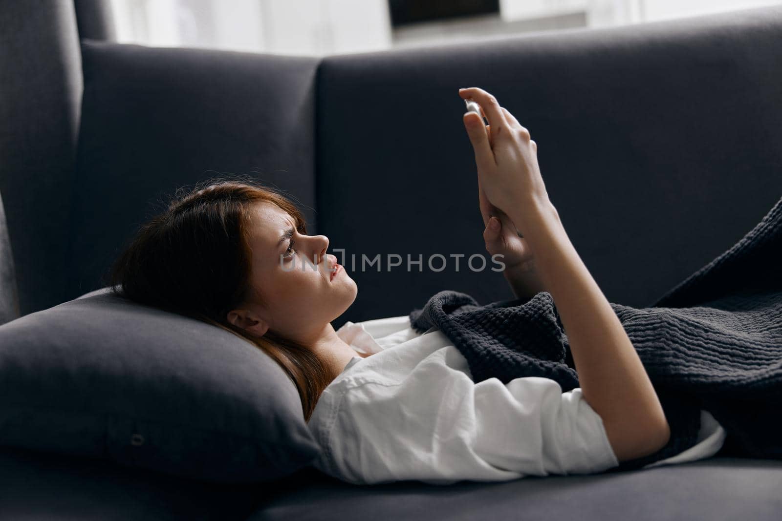 woman under the covers on the sofa and mobile phone in hand by SHOTPRIME