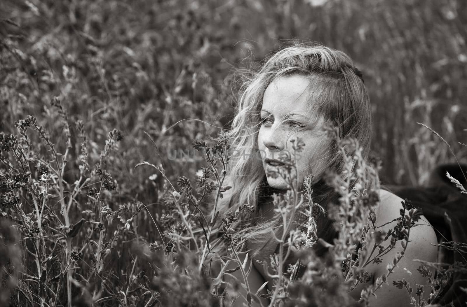 Black and white artistic portrait of freckled woman on natural background. Young woman enjoying nature among the flowers and grass. Close up summer portrait 