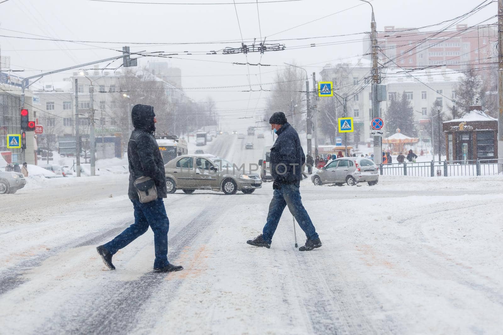Tula, Russia - February 13, 2020: Two men crossing city road during heavy snow fall at day light.
