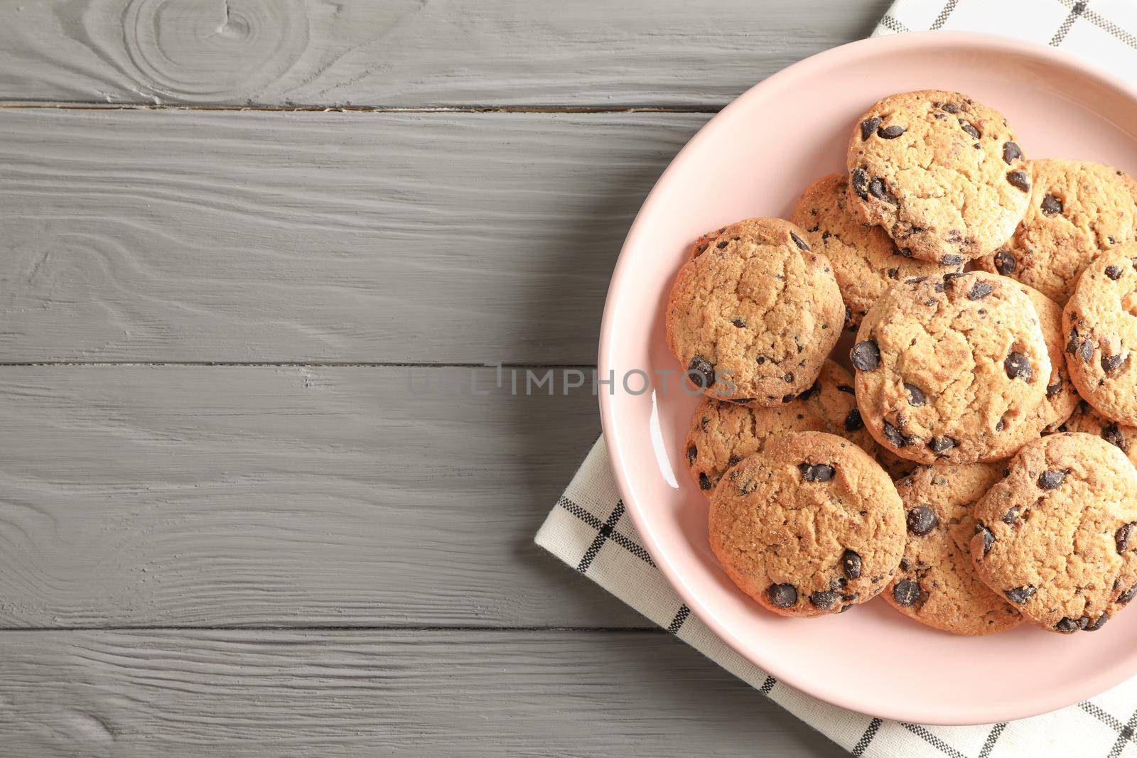 Plate with chocolate chip cookies and space for text on wooden table, top view