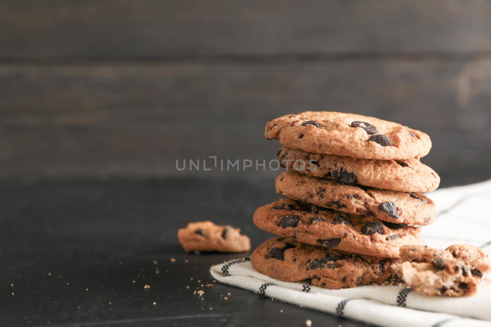 Stack of tasty chocolate chip cookies on napkin and wooden background. Space for text