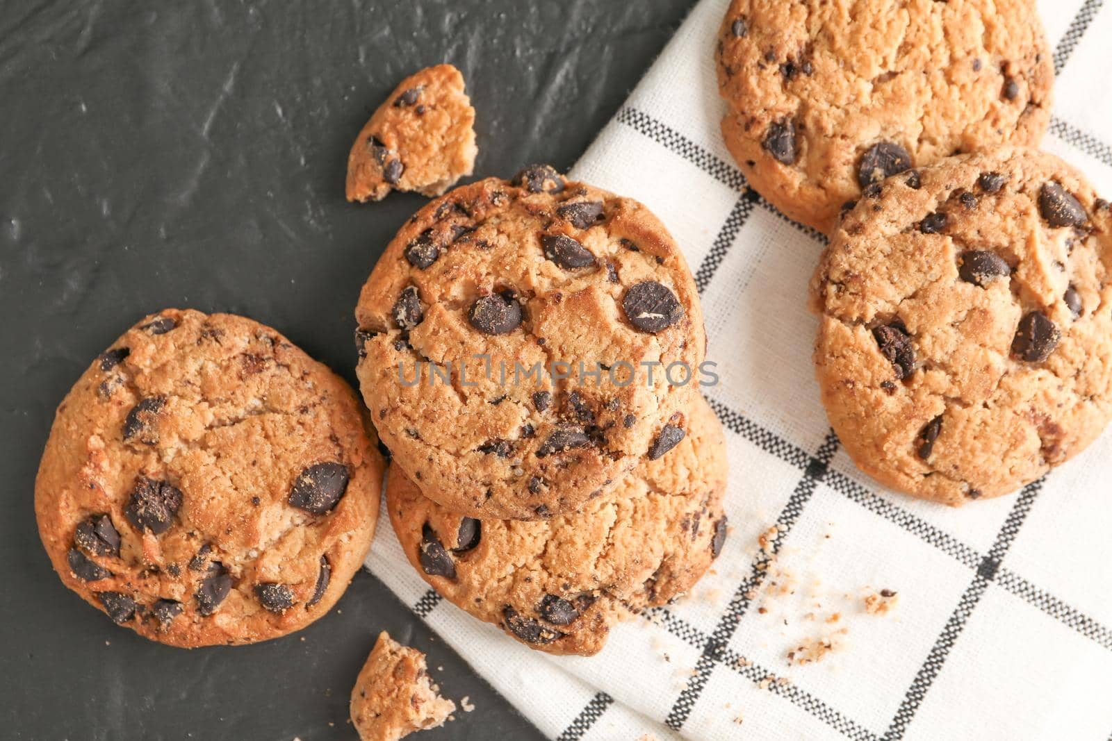 Stack of tasty chocolate chip cookies on napkin and wooden background, top view. Space for text