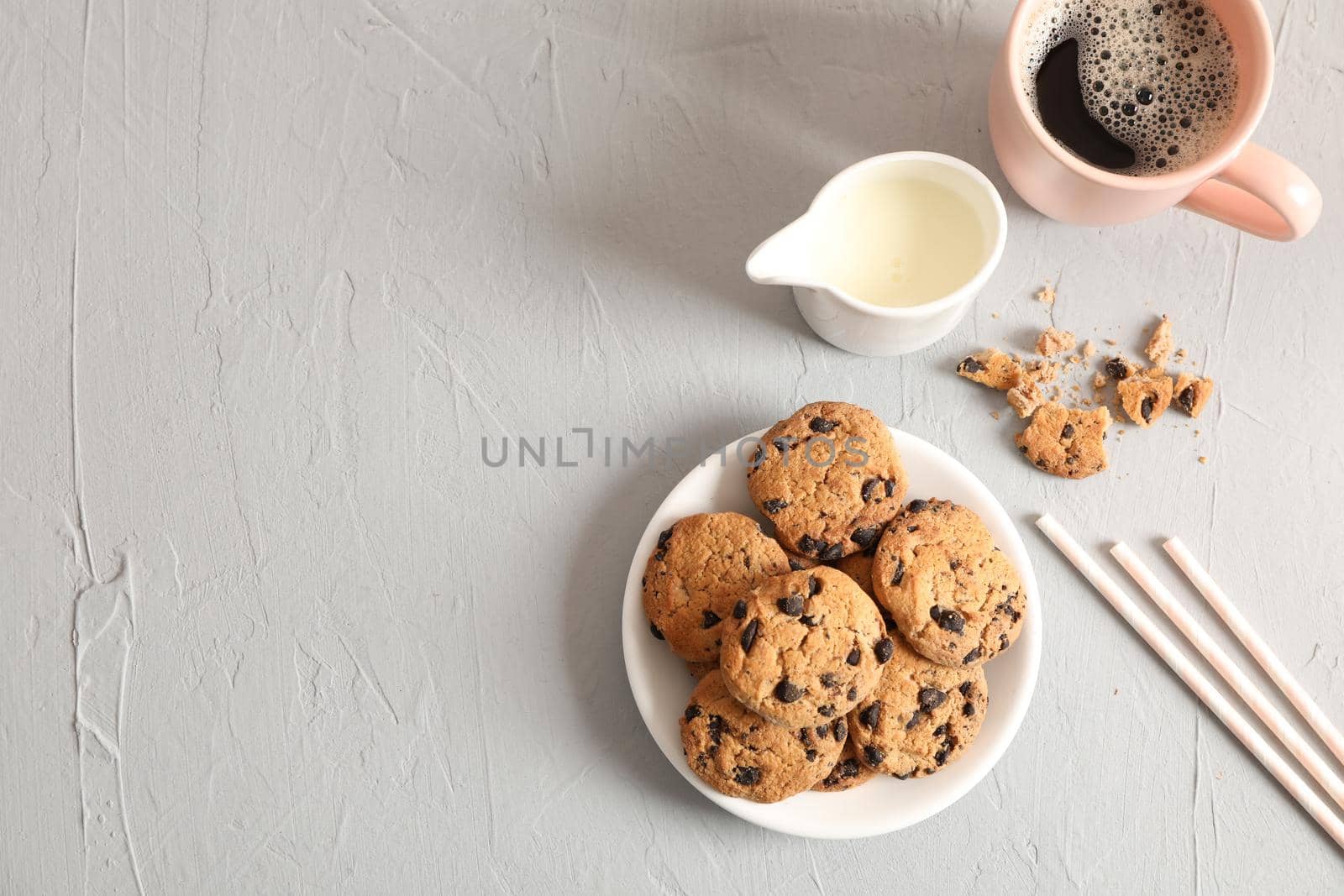 Plate with tasty chocolate chip cookies and cup of coffee on gray background, top view. Space for text