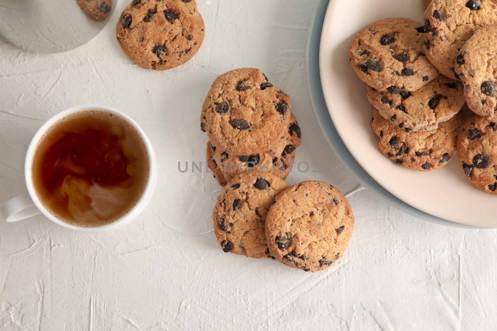 Plate with tasty chocolate chip cookies and cup of coffee on gray background, top view