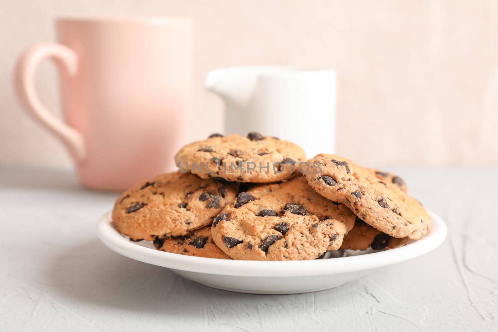 Plate with tasty chocolate chip cookies and blurred cup of milk on gray background, closeup by AtlasCompany