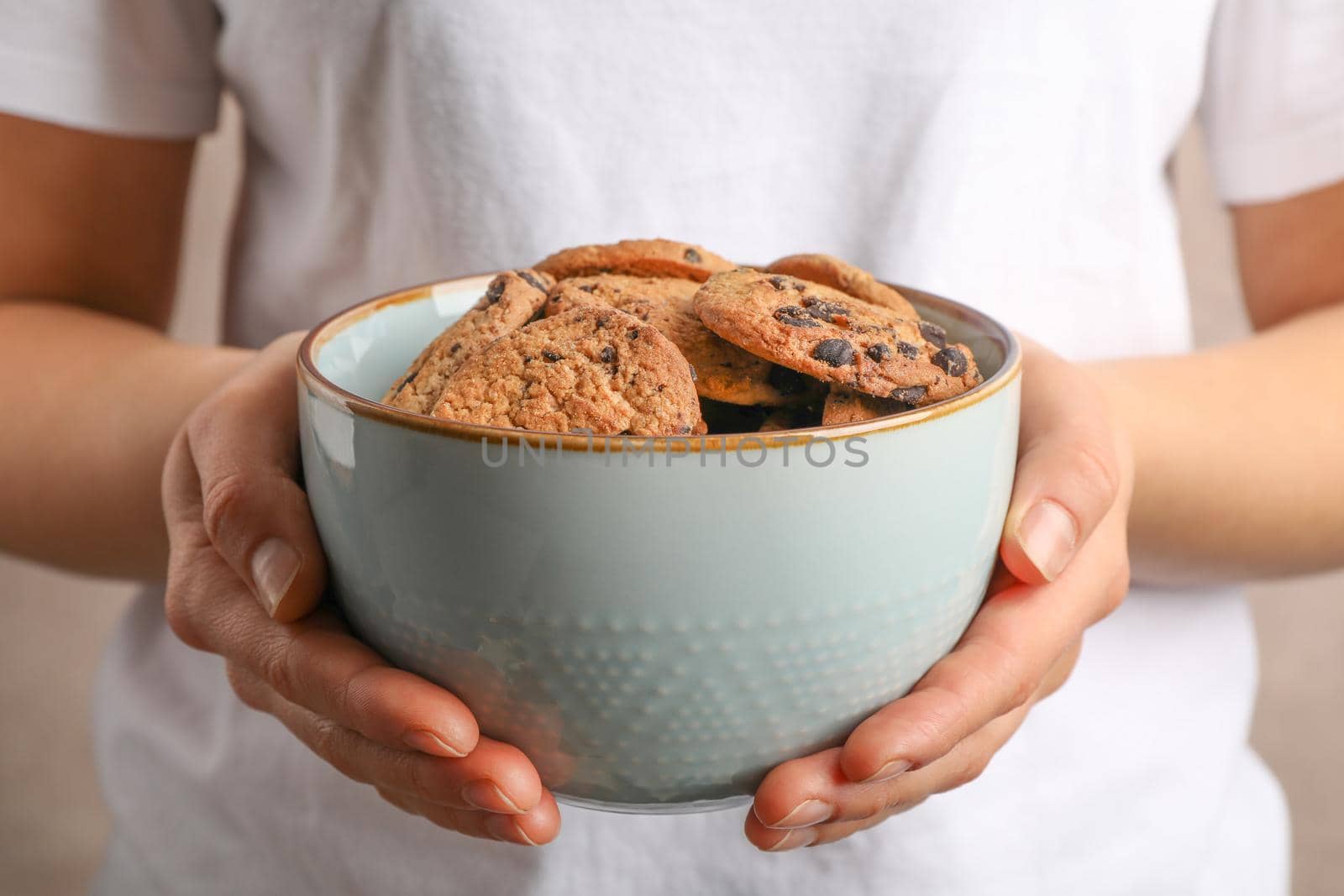 Woman holding bowl with tasty chocolate chip cookies, closeup by AtlasCompany