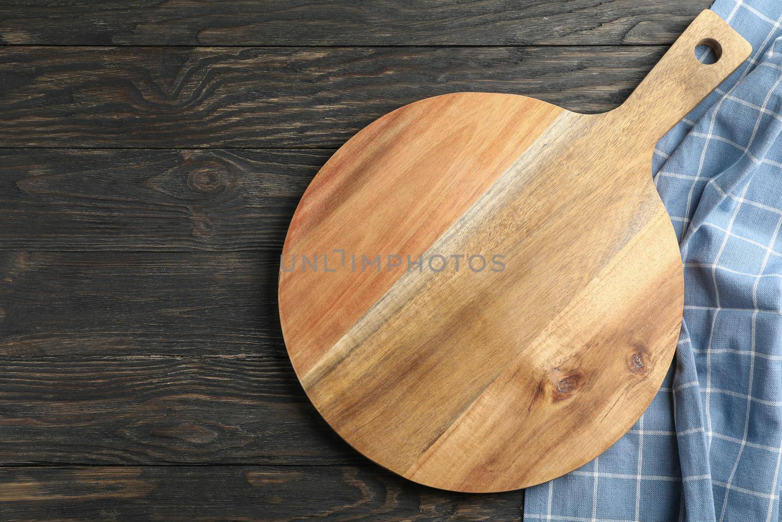 Cutting board with kitchen towel on wooden background, space for text