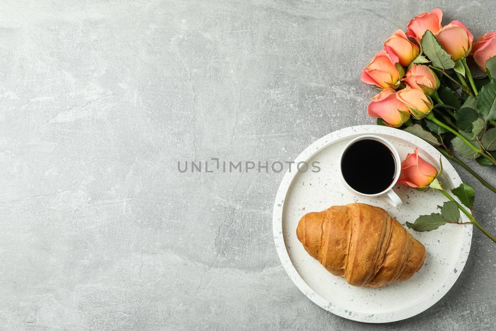 Composition with marble tray, cup of coffee, croissant, roses and space for text on grey background, top view by AtlasCompany